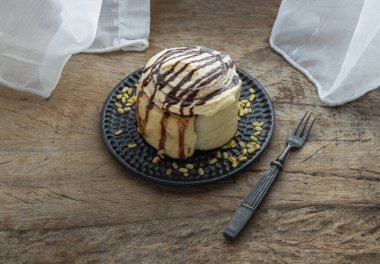 Cinnamon roll topped with rich cream cheese frosting served with Metal fork on old rustic wooden background. Homemade soft chocolate bun, The concept of delicious dessert, Space for text, Selective focus.