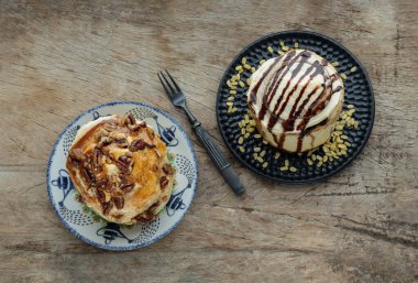 Two Homemade Soft Chocolate Buns, Cinnamon roll topped with rich cream cheese frosting and Caramel Pecanbon topped with caramel frosting and pecans served with Metal fork on old rustic wooden background. The concept of delicious dessert, Space for te