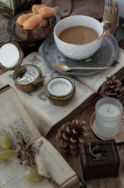 Morning refreshing with Hot coffee in ceramic cup and Fresh milk served with Sweet egg floss or Sweet egg floss (Foi thong) on old wooden worktable with old books, brass compass, coloured pencil, scented candle and dried flowers.