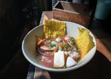 Yentafo egg noodles soup with pink sauce and Fish balls, Shrimp, Fresh squid, Fresh squid, Pickled squid, Jellyfish, Tofu and Fried wontons topped with chopped spring onions and coriander in Bowl. Traditional asian food style, Space for text, Selecti