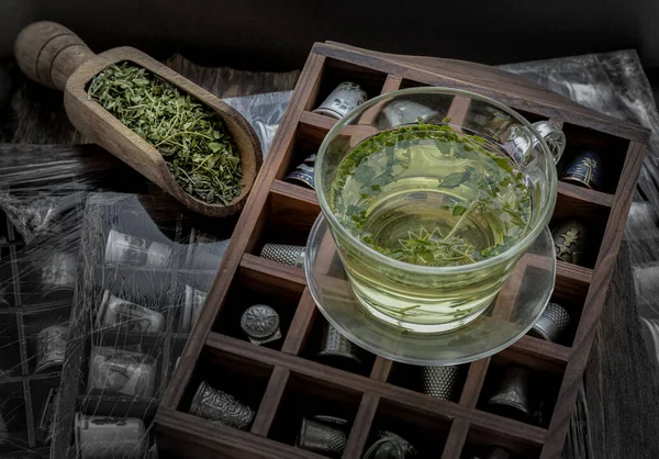 A cup of hot hemp tea (CBD herbal tea) and Dried organic hemp leaves placed on Vintage thimbles collection on an Old wooden boxs. Healthy drink concept. Dark tone, Space for text.