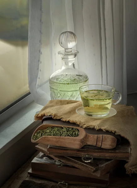 A cup of Hot Hemp Tea (CBD herbal tea) from Glass bottle with Dried organic hemp leaves placed on Sackcloth and old wood frames on wooden table by the window view with sunlight. Healthy drink concept. Space for text.