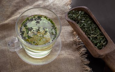 Relax time with A cup of Hot Hemp Tea (CBD herbal tea) from Dried organic hemp leaves in Wooden scoop on burlap placemat. Healthy drink tea at home.