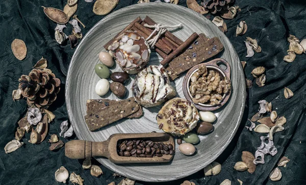Bakery, Stick cookies, Walnuts, Roasted coffee beans, Colored eggs and Pine cones on Ceramic plate with dark background. Easter desserts, Top view, Selective focus.