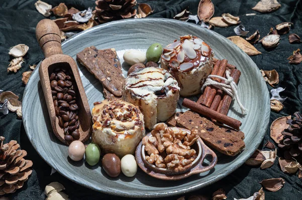 Bakery, Stick cookies, Walnuts, Roasted coffee beans, Colored eggs and Pine cones on Ceramic plate with dark background. Easter desserts, Selective focus.