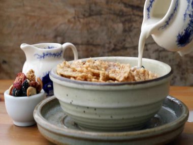 Tahta masada Tasty Gadola ile servis edilen seramik kasede mısır gevreğine süt dökmek. Sağlıklı kahvaltı kavramı, kopyalama alanı, seçmeli odak.