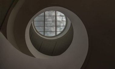 Yuvarlak yuvarlak tavanlı, sarmal merdivenli modern kanaldan gökyüzüne bakıyor. Ortasında büyük şeffaf cam panel olan beyaz tavan, gökyüzünü gösteren ana bir çatı penceresi, cam tavan, metin için boşluk, Seçici Odaklanma