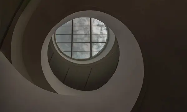 Looking up to the sky through modern channel round circular ceiling with spiral staircase. The white ceiling with Huge transparent circular glass panel on the middle as a main skylight showing sky above, Glass ceiling, Space for text, Selective Focus