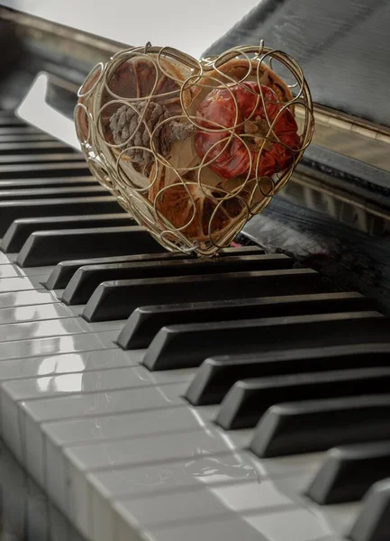 Golden heart shaped mesh case is filled with dried fruits stand on the Piano Keyboard. Dried fruits in heart shaped metal case on keyboard, Christmas decoration, Melody of Love concept, Space for text, Selective focus.
