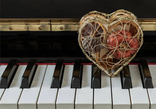 Golden heart shaped mesh case is filled with dried fruits stand on the Piano Keyboard. Dried fruits in heart shaped metal case on keyboard, Christmas decoration, Melody of Love concept, Space for text, Selective focus.