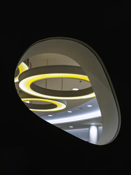 Looking through the Glass mirrored wall panels in the living room can see the hanging rounded ceiling mounted light fixtures with modern LED light bulb. See the yellow circular ring shaped lamps hanging under ceiling, Architecture and interior design