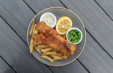 Otantik geleneksel İngiliz mutfağı Fish and Chips yanında patates kızartması, bezelye, limon ve tart sosunu seramik tabakta servis eder. Üst görünüm, metnin için boşluk, Seçici odak.