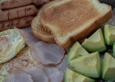 Kahvaltıda kızarmış sosis, sahanda yumurta, tost ekmeği ve avokado var. Metin için boşluk, Seçici odak.