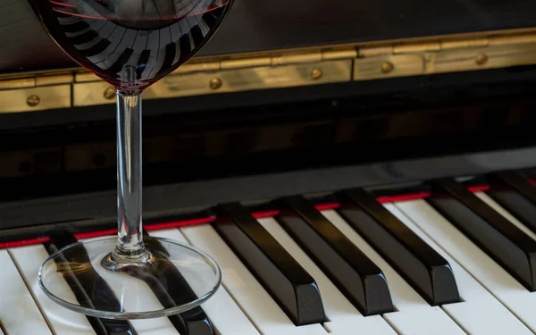 Glass of red wine on piano keyboard. Music and wine concept, Copy space, Selective focus.