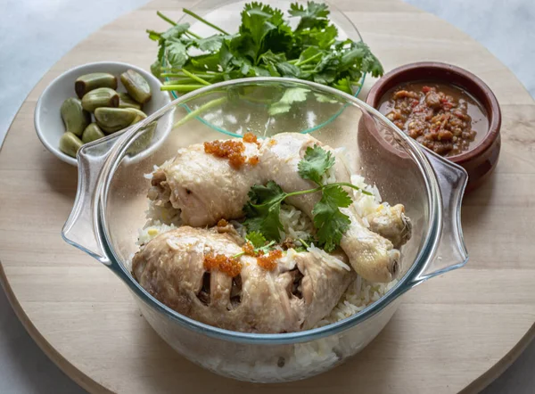 Delicious Steam chicken with rice (Hainanese chicken rice) serve with Pickled garlic, Cucumber and Chili sweet sauce on round wooden tray. Halal food, Copy space, Selective focus.