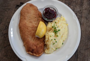 Pork Escalaope Viyana usulü saman domuz eti. Ev yapımı patates salatası, limon ve yaban mersini seramik tabakta servis ediliyor. Üst görünüm, metin için boşluk, Seçici odak.