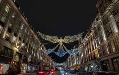 Londra, İngiltere - 25 Aralık 2023 - Uçan melek Noel süslemesi ışık gösterimine öncülük etti. Alacakaranlıkta Regent Caddesi 'nin üzerinde asılı geleneksel Noel süsleme ışıklarının dramatik manzarası, Noel Ruhu, Londra' da Işık Festivali, Seçici odak