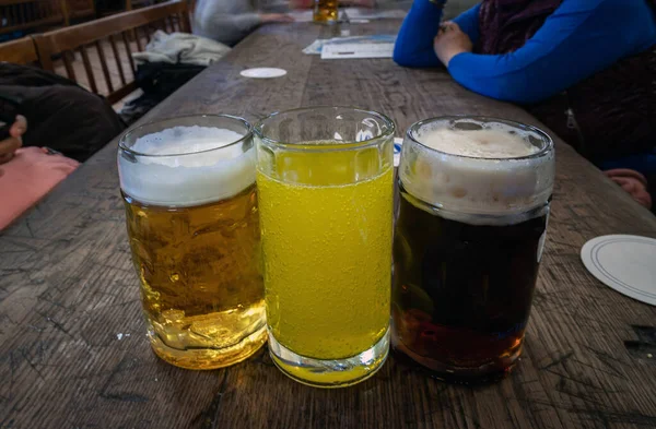 Three glasses of different types of cold tasty beer are in a row on a wooden table in a restaurant. Table for company of friends, Space for text, Selective focus.
