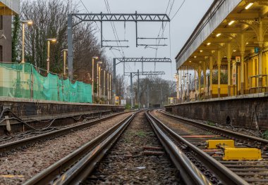 Londra, İngiltere - 25 Aralık 2023 - Boş demiryolu rayları ve elektrik altyapı ekipmanlarına perspektif görüşü, Acton merkez tren istasyonunda kablolar. Tren peronunun metal çerçeveli demiryolu sistemi, nakliye ve nakliye peyzajı konsepti, Demiryolu