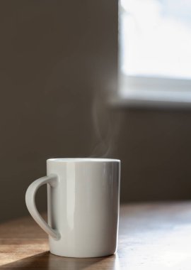 Yalnız beyaz bir kahve fincanı, sabah vakti, pencerenin yanındaki ahşap bir masanın üzerinde oturur. Sabah kahve fincanından çıkan buhar, yalnızlık ve minimalizm kavramı, metin için yer, seçici odaklanma..