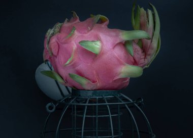 Yalnız bir ejderha meyvesi ya da pitaya siyah arka planda zeytin yeşili bir kafes takar. Boşluğu kopyala, Seçici odak.