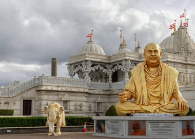 London, UK - Feb 23, 2024 - The gold colored statue of spiritual leader holiness pramukh swami maharaj front of Neasden temple (BAPS Shri Swaminarayan Mandir) against a nice cloudy sky background. Hindu temple in Neasden to build is constructed from  clipart
