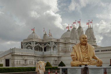 London, UK - Feb 23, 2024 - Exterior view of the Neasden temple (BAPS Shri Swaminarayan Mandir) and The gold colored statue depicts the late spiritual leader Pramukh Swami Maharaj against a nice cloudy sky background. Hindu temple in Neasden to build clipart