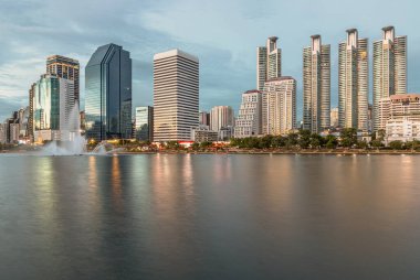 Bangkok, Tayland - 22 Haziran 2024 - Cityscape ofis binaları su yüzeyine yansıyan modern mimari ile. Gün batımından önce gökdelenlerin ve dramatik gökyüzünün resimli görüntüsü, metin için boşluk, seçici odak.