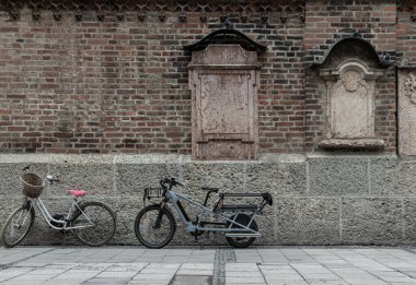 Münih, Almanya - 21 Aralık 2023 - Münih Frauenkirche ya da Frauenkirtz Katedrali 'nin (Leydimizin Katedrali) dış duvarına dayanan Atlı mezar taşlarının yanında uzun kuyruklu ve elektrikli bisiklet park halindedir. 