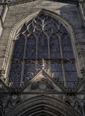Edinburgh, İskoçya - 18 Ocak 2024 - Güneş lekeli cam kemerli pencerelerin yüzeyinden parlıyor ve Gable, Edinburgh 'daki St. Giles Katedrali' nin giriş kapısının üzerinde. High Kirk 'ün Neo-gotik' teki dış mimari detayları.. 