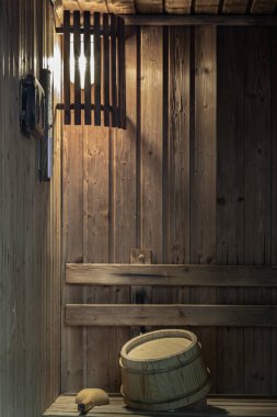 Mekan, ahşap kovanın ve kepçenin üzerine, ahşap bankların ve duvarların üzerine serpiştirilmiş, duvara monte edilmiş bir lambayla sıcak bir şekilde aydınlatılıyor. Küçük ahşap bir sauna iç odası, rahatlama spa konsepti. Sıcak bir saunada rahatlayın, metin için boşluk, seçici odak