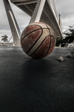 Basketball ball on the Old cement court floor at Outdoor park with Suspension bridge and Sky in the background. Space for text, Selective focus. clipart