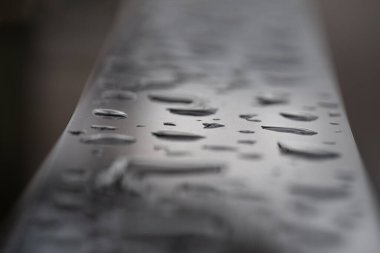 Metalik yüzeydeki yağmur suyu damlalarını kapatın. Yağmur damlacıkları paslanmaz çelik sapına tünemiş, doğal yağmur damlaları ya da duvar kağıdı posteri ve afiş tasarımı için gümüş metal zemin üzerine çiğ damlaları, seçici odak noktası.