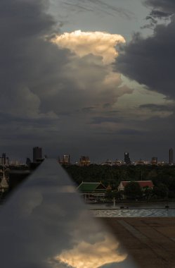 The sky is being covered with amazing clouds with reflection on stainless steel handrail with city view alongside river. Concept idea of Imaginative clouds background, Nature abstract composition for wallpaper and text, Selective focus. clipart