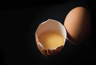 Kırık yumurta sarısı ve yumurta kabuğuyla yumurta sarısı ve siyah arka planda taze tavuk yumurtası. Çiftçiden taze yumurta, doğal organik sağlıklı gıda konsepti, yazı için alan, seçici odaklanma..