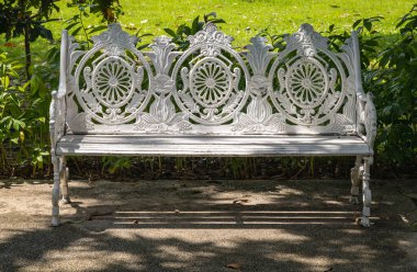 Boş, süslü, antika bir antikanın arka planda kalan güneş ışığı sessiz park alanının gölgeli bir bölgesinde demir bir bank oluşturdu. Şehir parkında, oturma ve gevşeme alanında, Aydınlık ve Gölge, yazı için alan, seçici odak noktasında, beyaz boya dökme demir Victoria tarzı bahçe tezgahı.