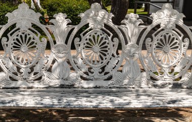 Details of White painted cast iron victorian style garden bench in city park. Sunlight on backrest surface of Empty ornate antique cast iron bench in a shady area of the quiet park area, Seat and unwind area, Light and Shadow, Copy space, Selective f clipart