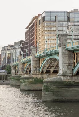 Londra, İngiltere - Nov 07, 2023 - Southwark Köprüsü manzarası (eskiden Queen Street Bridge olarak bilinir) Thames Nehri 'ni arka plandaki modern binalarla geçer. Turkuaz dökme demir kemer köprüsü, seçmeli odak.