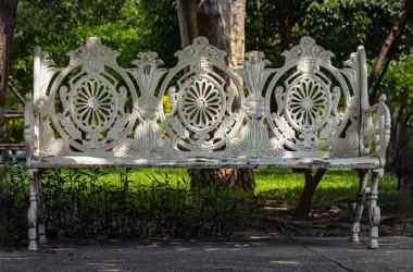 One empty bench made of white iron stands on city park. Sunlight on backrest surface of Victorian pattern white cast iron garden bench in a shady area of the quiet park area, Seat and unwind area. Light and Shadow, Copy space, Selective Focus. clipart