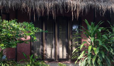 Nakhon Ratchasima, Tayland - 20 Mar, 2022 Sersemletici ahşap ev, cam pencereler ve güneşli bir günde yemyeşil ile çevrili Thatched çatı. Yazı için duvar kağıdı, poster ve boşluk olarak kullanın. Seçici odak.