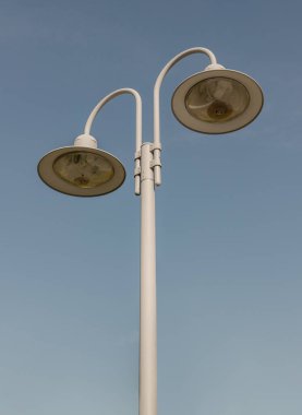 Sabaha kadar mavi gökyüzünün arka planında beyaz metal lambaların üzerinde iki klasik sokak lambası olacak. Metin, Seçici odak için Duvar Kağıdı, Poster ve Boşluk olarak kullan.