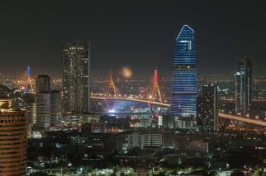 Bangkok, Tayland 31 Aralık 2024 Bhumibol Köprüsü üzerinde renkli havai fişeklerle gökdelenlerin gece görüşü. Güzel şehir Bangkok 'ta yeni yılın parlak ışıkları havai fişekleri kutluyor. Duvar kağıdı, poster ve boşluk olarak kullanın.