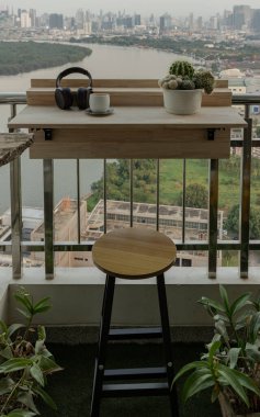 Bangkok, Tayland 02 Ocak 2025, ayarlanabilir balkon masası ve tahta sandalyeli balkon. Nehir manzaralı Condominium balkonunda rahatlama alanı, kulaklıklı rahat bir yer, Katlanan güverte demiryolu masasında çay fincanı ve kaktüs tenceresi.