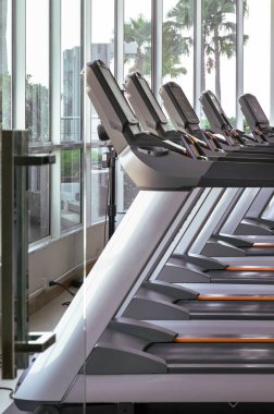 Bangkok, Tayland - 18 Ocak 2025 - Koşu bandından güneş ışığının spor salonuna girdiği sabah manzarası. Spor salonundaki koşu bandı makinelerinin yan görüntüsü. Duvar kağıdı, poster ve kopyalama alanı olarak kullanın. Seçici odak noktası..