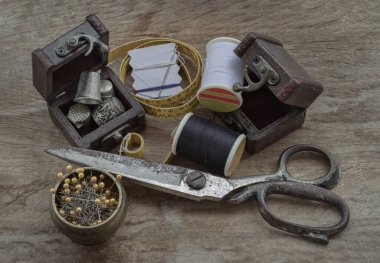 Beyaz bir kağıda sıkışmış iğneler, küçük ahşap hazine sandığında yüksükler, siyah beyaz iplik makaraları, çelik makas ve tahta masadaki pirinç kaptaki raptiyeler de dahil olmak üzere mezura. Nesneler ayarlanıyor ya da Dikiliyor (kavramları dikiş), kullanın 