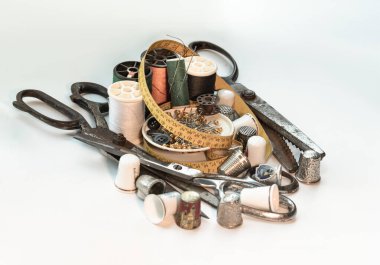 Çelik makas, yüksük, çeşitli renkte iplik makaraları, yeşil minyatür makaralara saplanmış iğneler, iğne ipliği ve mezura şeritleri, beyaz zemin üzerinde küçük yuvarlak tepsi içinde küçük yuvarlak tepsiler. Dikiş ögeleri seti veya dikiş kavramları (ob dikme