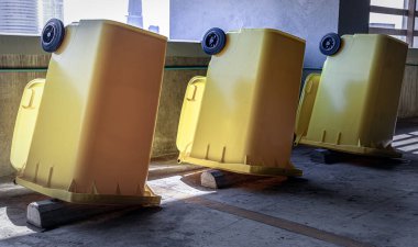 Büyük plastik çöp konteynırını temizledikten sonra kuruyana kadar baş aşağı çevirme görüntüsü. Dairenin otoparkındaki beton duvarın yanındaki büyük, sarı plastik çöp kutusu, genel atık için kapağı olan plastik çöp, duvar kağıdı olarak kullanın..