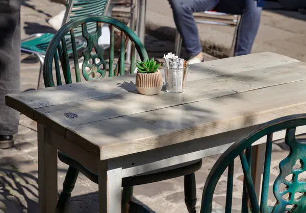 Windsor, İngiltere - Nisan 03, 2025 - Gün ışığı ahşap masa boyunca parlıyor ve öğleden sonra bir kafede yeşil metal sandalyeler var. Metin, Seçici odak için Duvar Kağıdı, Poster ve Boşluk olarak kullan.