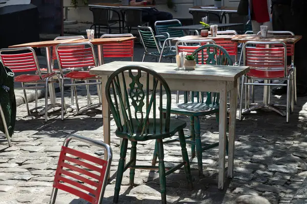 Windsor, İngiltere - Nisan 03, 2025 - Gün ışığı ahşap masa boyunca parlıyor ve öğleden sonra bir kafede yeşil metal sandalyeler var. Metin, Seçici odak için Duvar Kağıdı, Poster ve Boşluk olarak kullan.