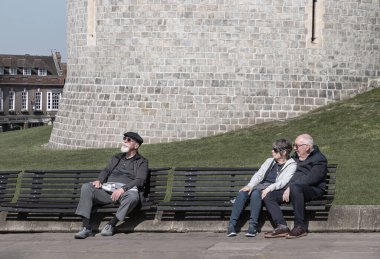 Windsor, İngiltere - Nisan 03, 2025 - Windsor kalesinin önündeki ahşap bankta oturan yaşlı insanlar. Emeklilik süresi ve yaşam tarzı, bunu metin, seçici odak için duvar kağıdı, poster ve boşluk olarak kullanın.